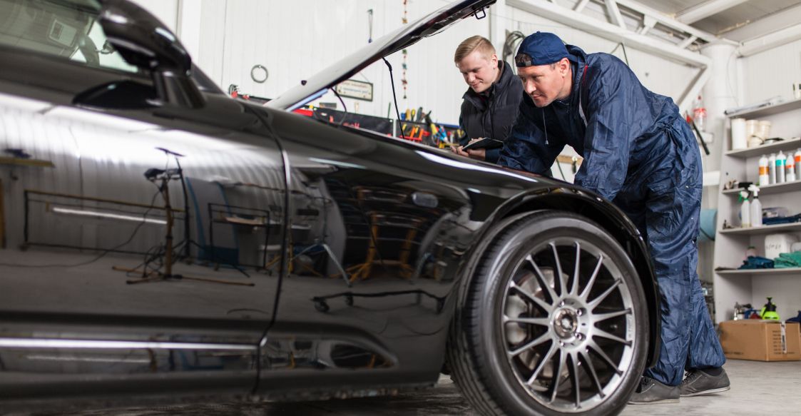 Zwei Männer in blauen Overalls arbeiten an einem Auto in einer Werkstatt