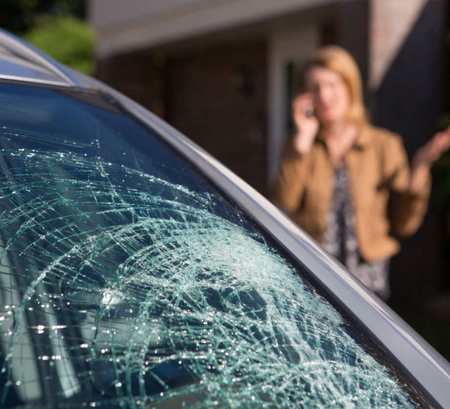 Eine Frau spricht am Handy neben einem Auto mit zerbrochenem Windschutzscheibe